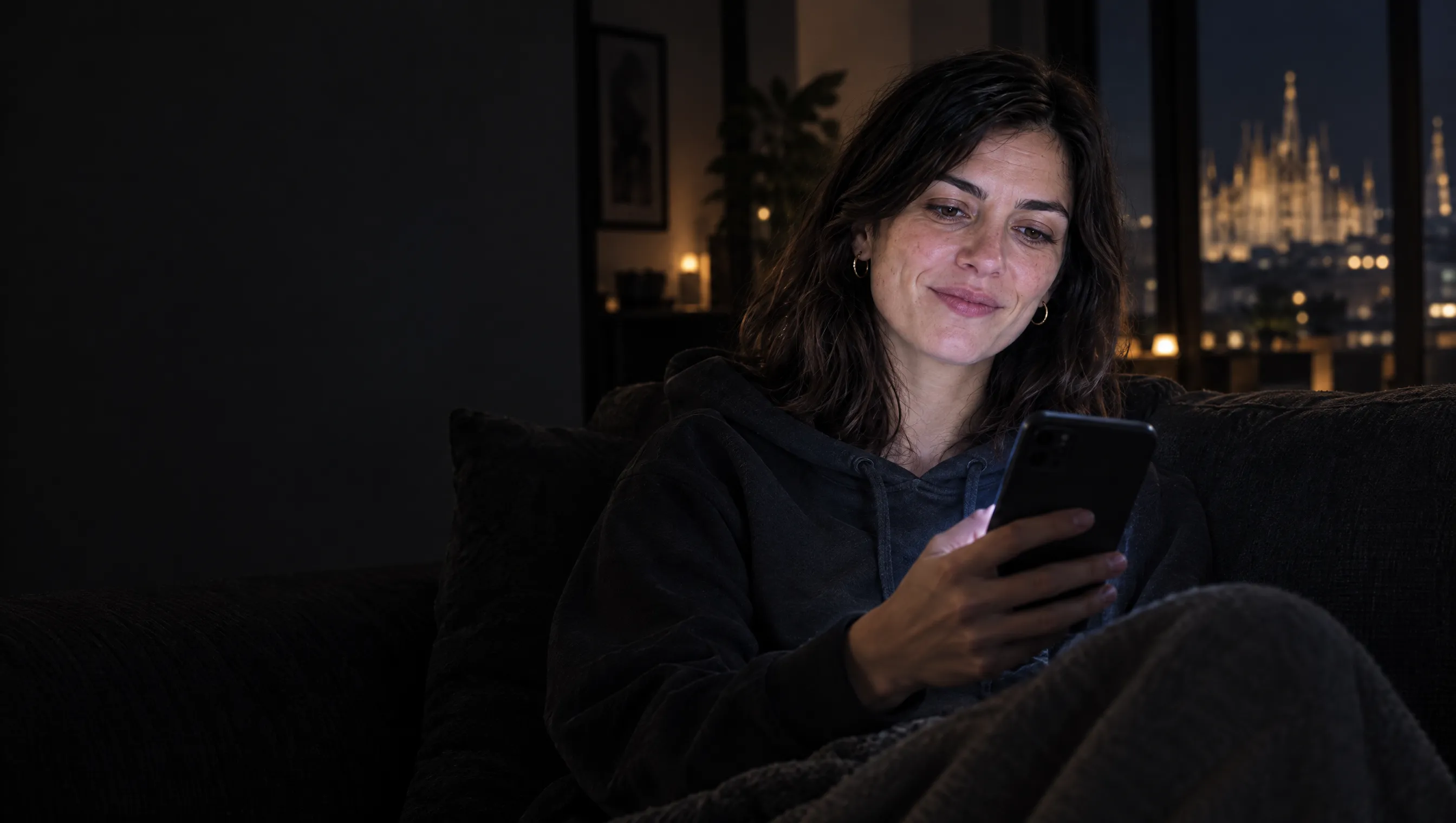 Lei sul divano al buio, il telefono acceso in mano